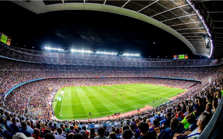 Wide view of a packed football stadium under floodlights during a match