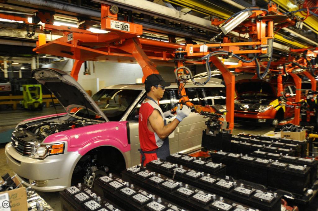 Automotive assembly worker operating production equipment beside vehicles on a factory assembly line
