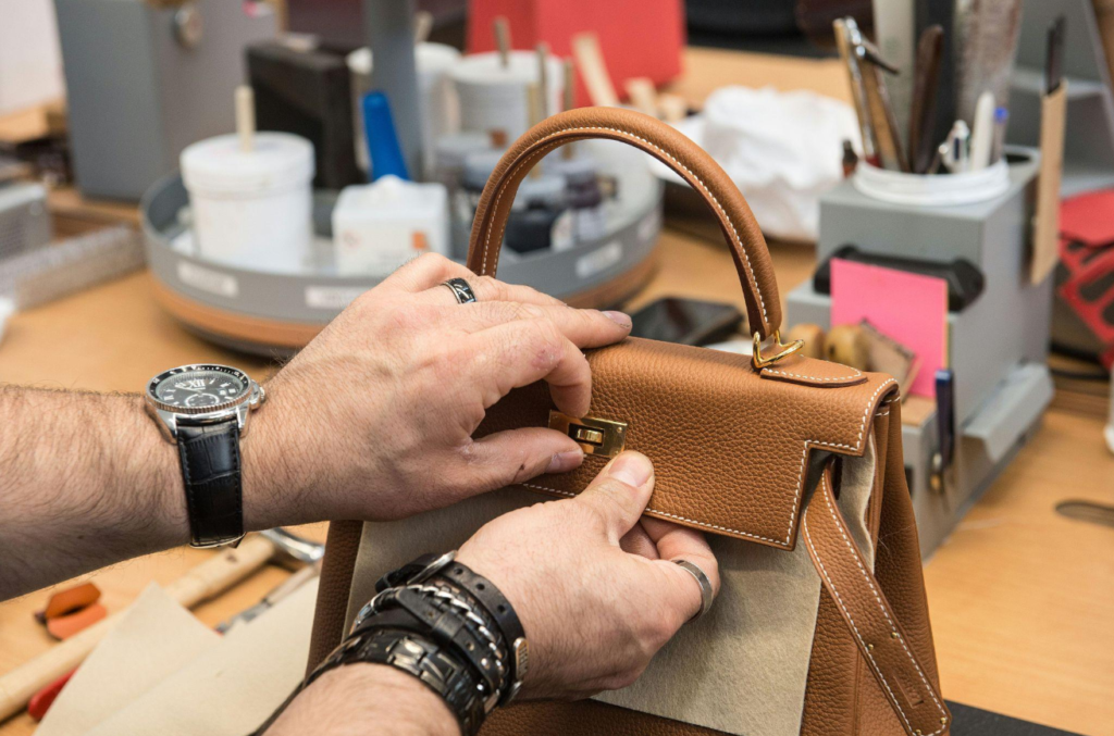 Artisan carefully stitching leather goods inside a luxury workshop.