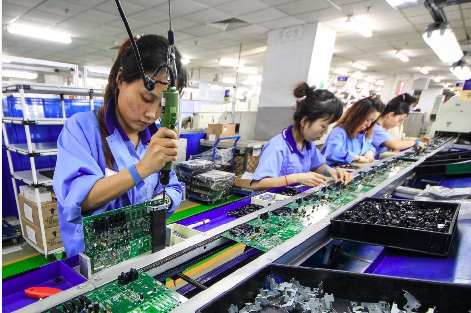 Workers assembling electronic components at a physical manufacturing workstation.