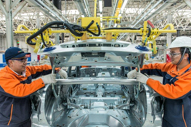 Two automotive factory workers handling a vehicle body on an automobile assembly line.