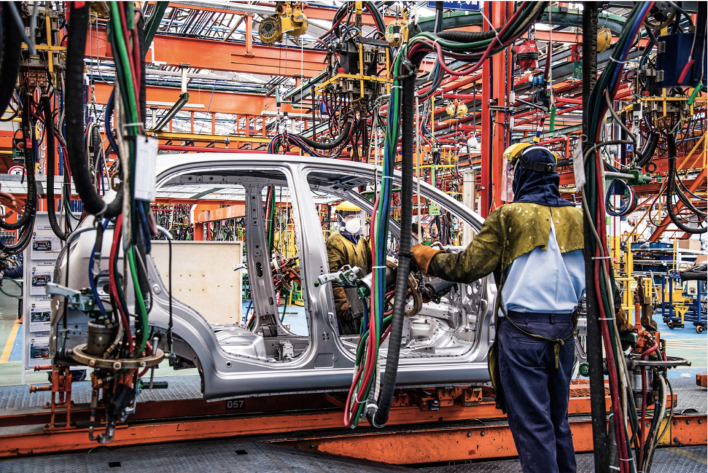 Workers assembling vehicles inside an automobile manufacturing facility.