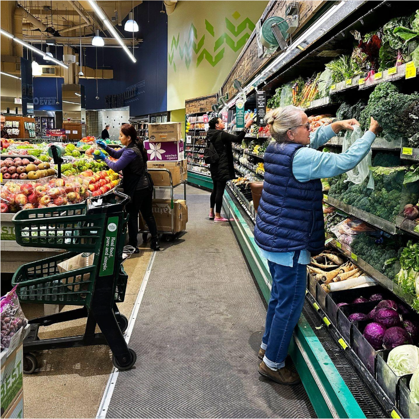 Shoppers selecting fresh vegetables inside a supermarket produce section.