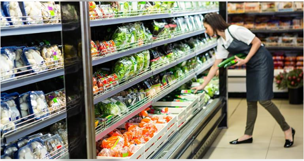 Supermarket employee stocking fresh produce on grocery store shelves.