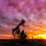 Silhouette of an oil pumpjack against a dramatic sunset sky