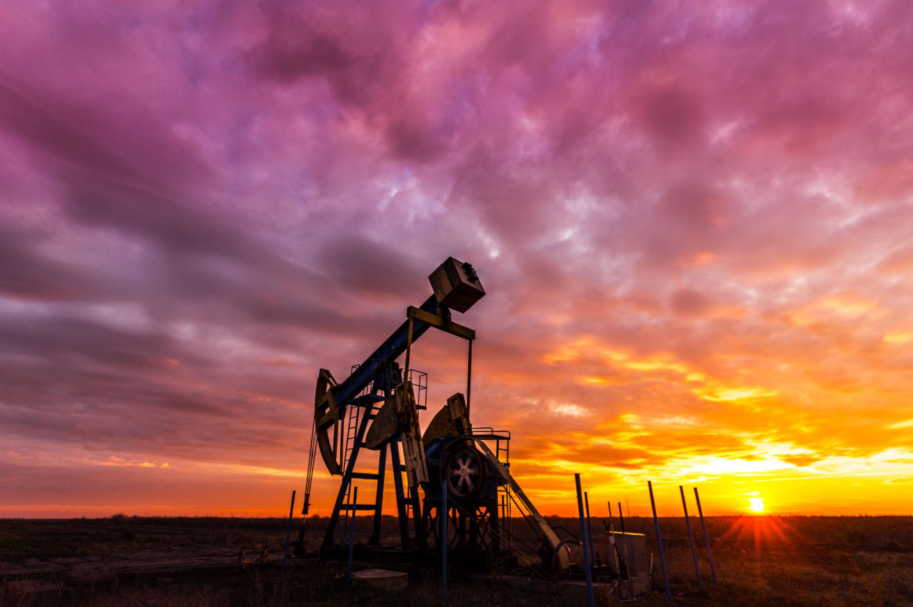 Silhouette of an oil pumpjack against a dramatic sunset sky