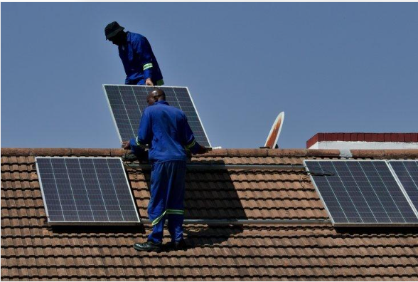 Two technicians installing solar panels on the roof of a building.